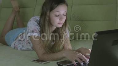 漂亮的女孩躺在沙发上用他的笔记本电脑工作。 她在智能<strong>手机</strong>上<strong>接电话</strong>。